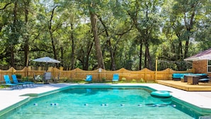 A swimming pool with clear water, surrounded by blue lounge chairs and a wooden fence. - Lrge Golden Isles Home-Huge Pool, Hot Tub, Game Rm (Brunswick)