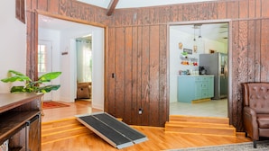 A room with wooden paneling, a ramp, a brown leather chair, and a kitchen in the background. - Lrge Golden Isles Home-Huge Pool, Hot Tub, Game Rm (Brunswick)