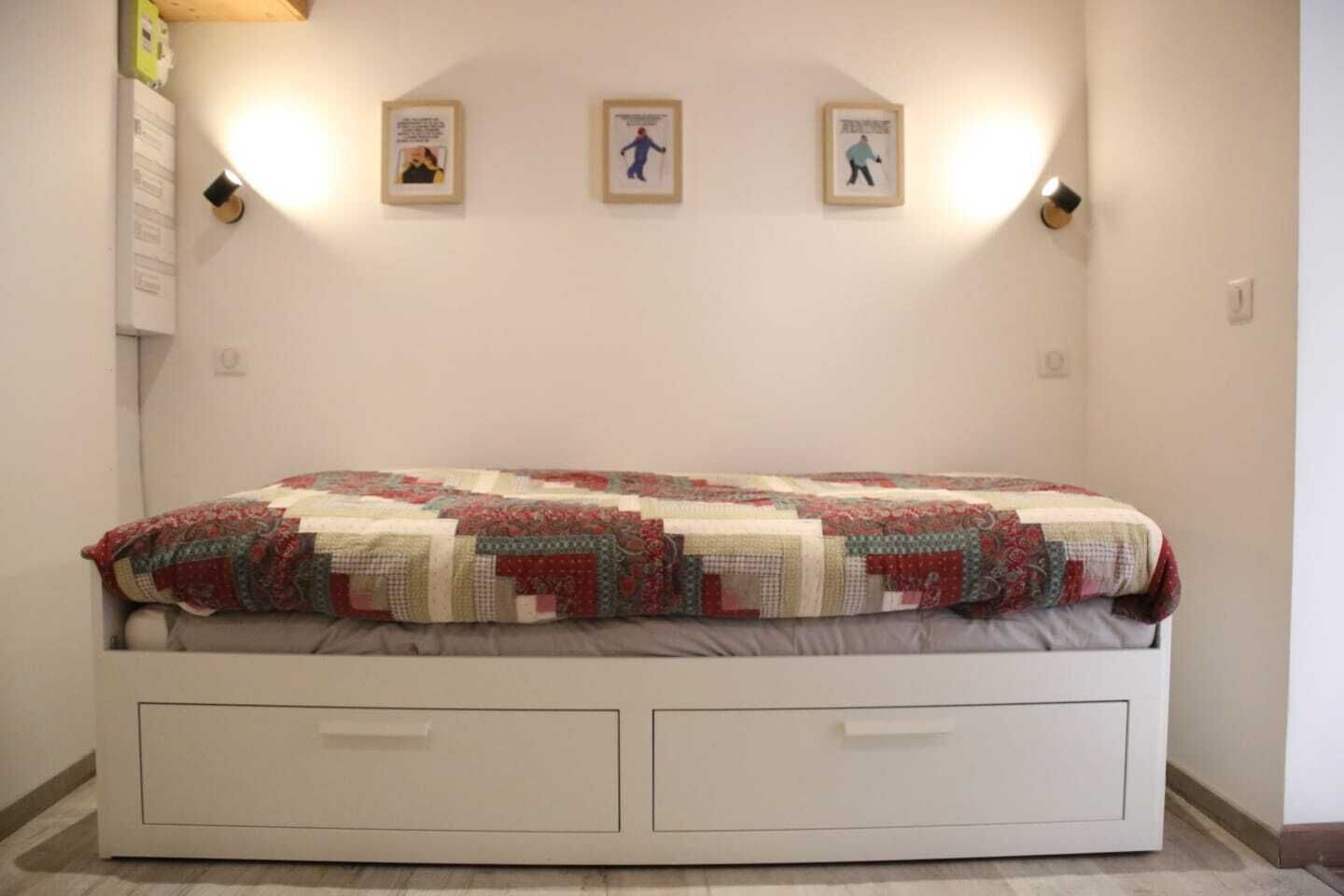 A bedroom with a bed, a quilt, and three framed pictures on the wall.