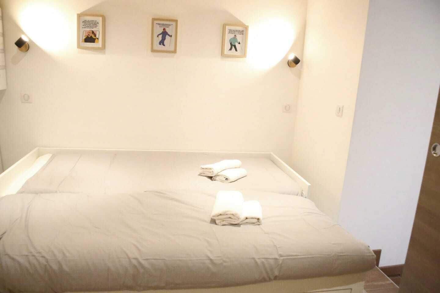 Una cama bien hecha con toallas dobladas, una pared de color claro y tres cuadros colgados sobre la cama.