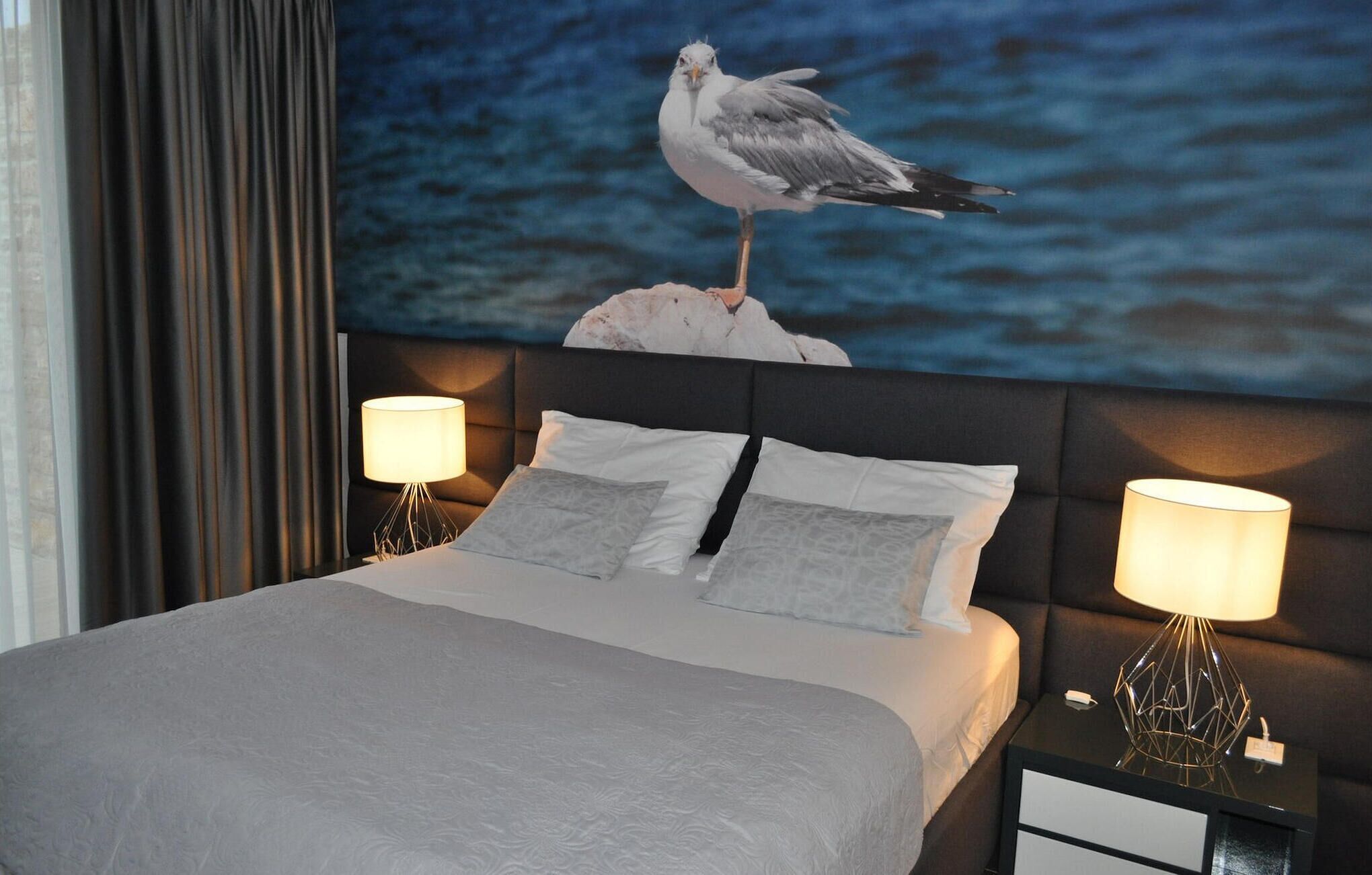 Ein Hotelzimmer mit einem Bett, zwei Nachttischlampen, einem Nachttisch und einem großen Wandbild einer Möwe.