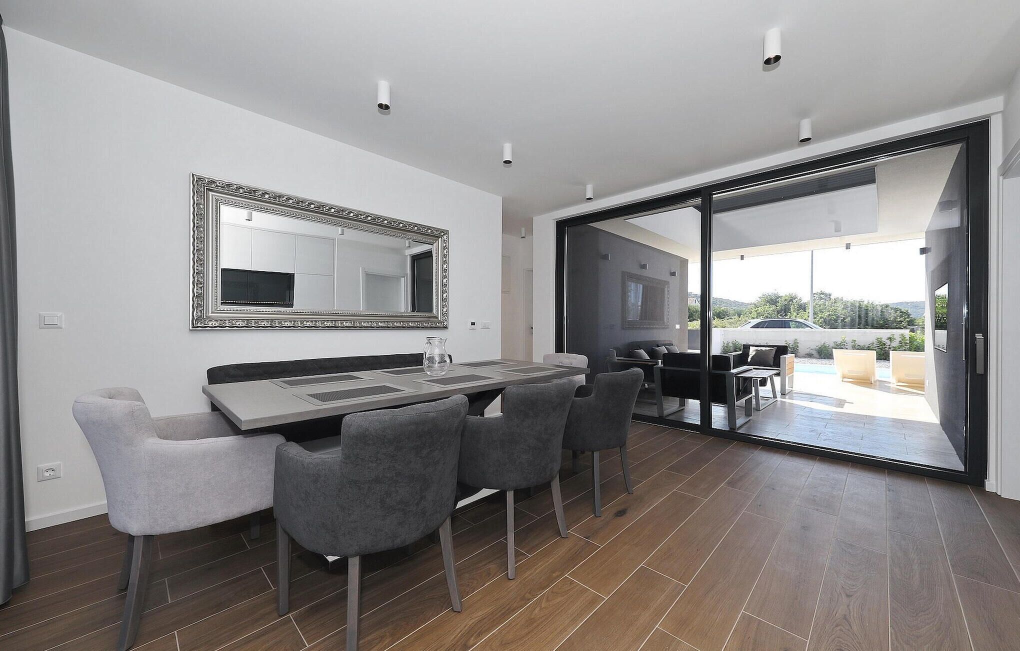 A modern dining area with a large table and chairs, a decorative mirror, and a sliding glass door leading to an outdoor space.