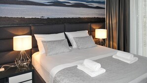 Une chambre d’hôtel avec un lit, deux lampes de chevet, une vue sur un lac et des montagnes, et un rideau à la fenêtre.