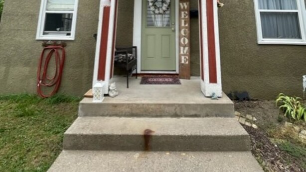 Une maison à deux étages avec un porche à l’avant, une porte verte et une pancarte indiquant « Bienvenue ».
