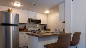 Una cocina moderna con armarios blancos, electrodomésticos de acero inoxidable y una isla central con dos sillas marrones.