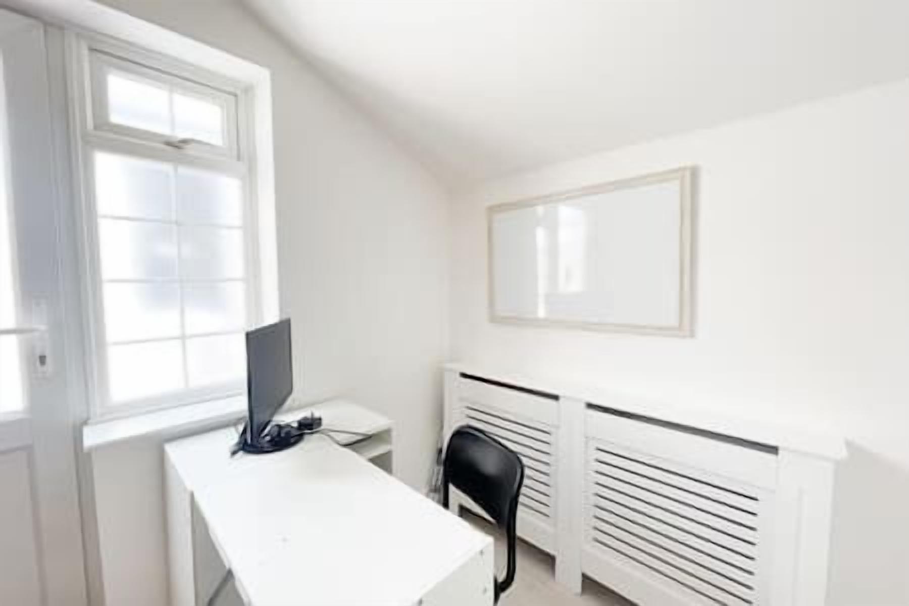A small, white room with a desk, a chair, a window, and a radiator.