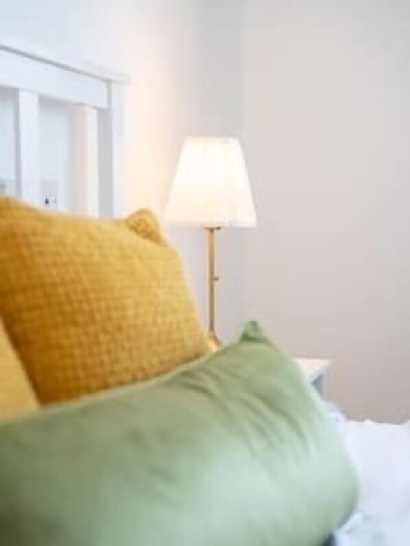 A bed with yellow and green pillows, a white headboard, and a bedside lamp.