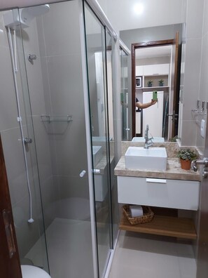 A bathroom with a glass shower enclosure, a sink with a marble countertop, and a mirror above the sink. - Encantadora casa em Ponta Negra (Natal)