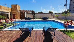 A swimming pool with lounge chairs, a wooden deck, and a pergola. - Encantadora casa em Ponta Negra (Natal)