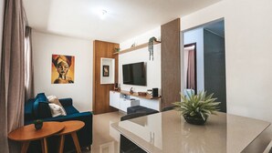 A modern living room with a flat-screen TV, a sofa, a coffee table, and a dining table. - Encantadora casa em Ponta Negra (Natal)
