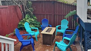 Eine Terrasse mit Backsteinboden, umgeben von einem roten Holzzaun, mit einem Tisch und sechs türkisfarbenen Stühlen.