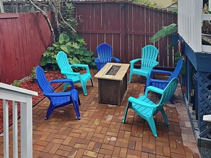 Une terrasse avec un sol en briques, entourée d’une clôture en bois rouge, comprenant une table et six chaises turquoise.