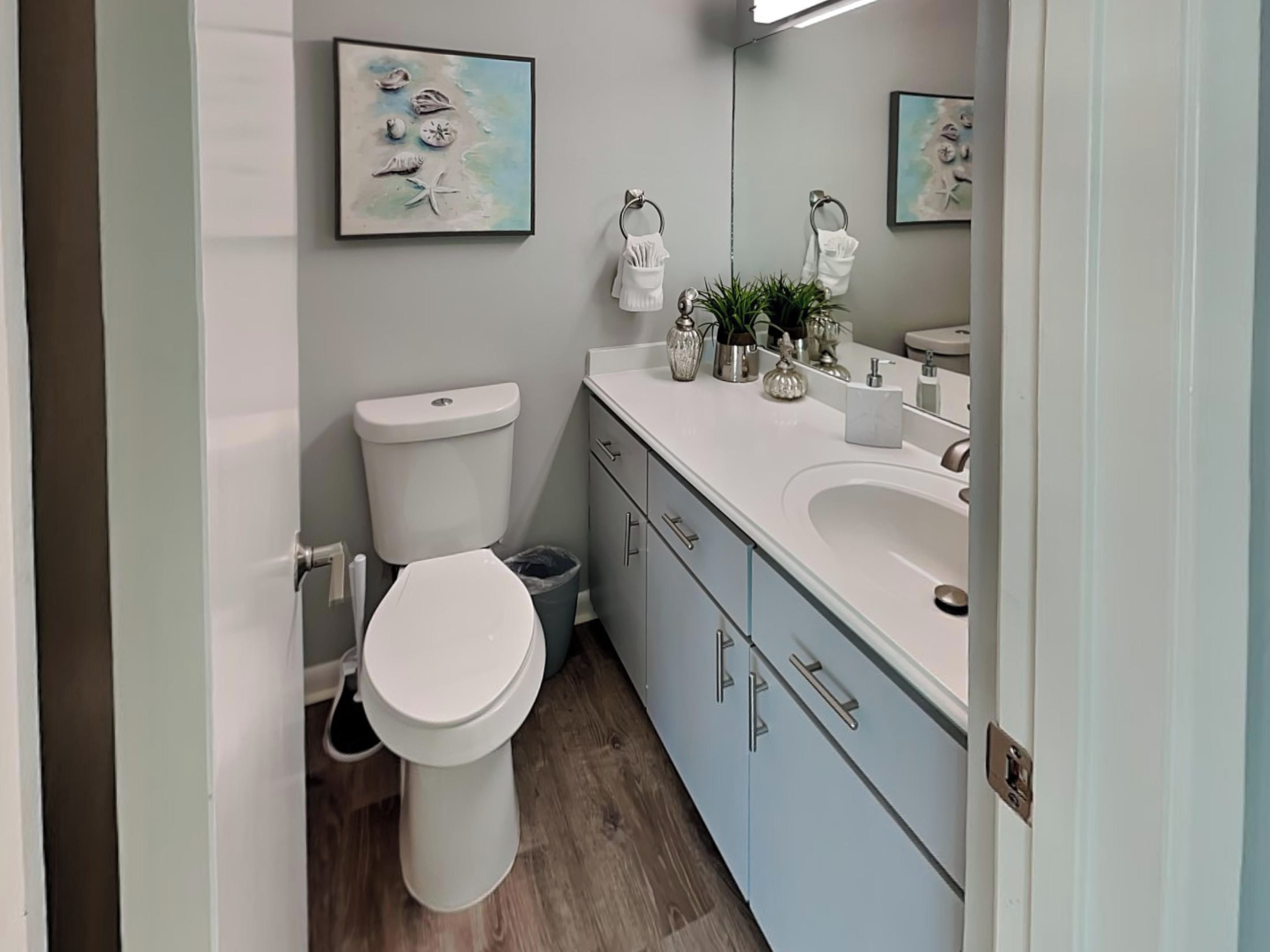 Un baño moderno con inodoro, lavamanos y armarios. Hay objetos decorativos en la encimera y un cuadro en la pared.