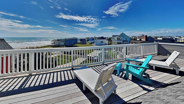 A wooden deck with lounge chairs and a view of the ocean and houses. - Pirates' View of the Sea by Ryson Vacation Rentals (Galveston)