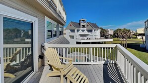 A wooden deck with a single Adirondack chair, a white railing, and a view of a white building with a balcony. - Pirates' View of the Sea by Ryson Vacation Rentals (Galveston)