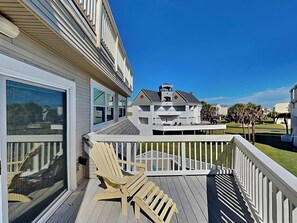 A wooden deck with a single Adirondack chair, a white railing, and a view of a white building with a balcony. - Pirates' View of the Sea by Ryson Vacation Rentals (Galveston)