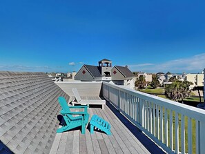 A wooden deck with two turquoise chairs, a gazebo, and a view of a residential area with houses and a beach. - Pirates' View of the Sea by Ryson Vacation Rentals (Galveston)