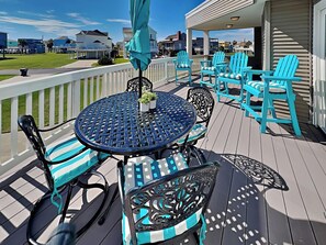 A covered outdoor deck with a round table and chairs, a white picket fence, and houses in the background. - Pirates' View of the Sea by Ryson Vacation Rentals (Galveston)