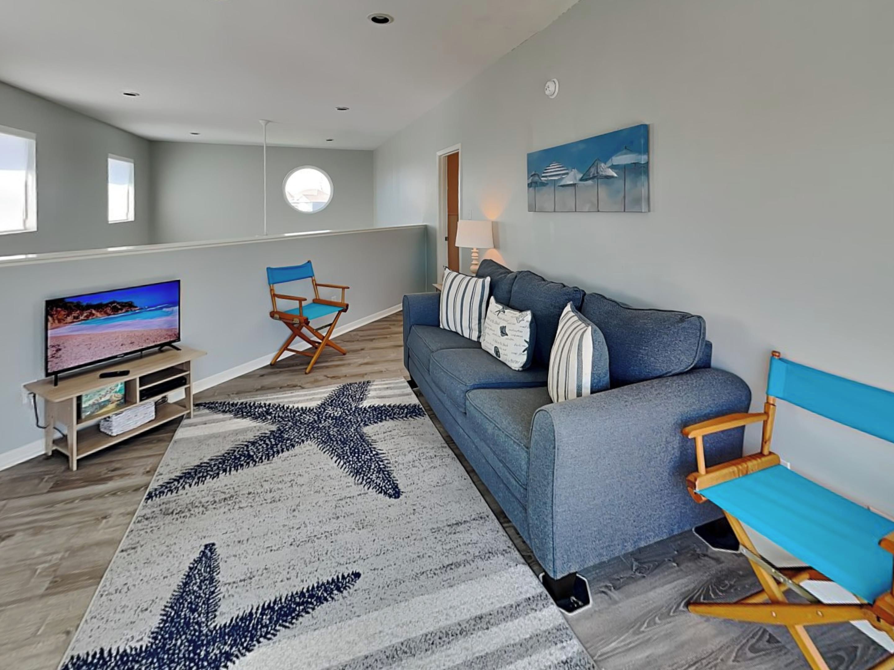 Un salon moderne avec un canapé bleu, un tapis à motifs étoilés, un téléviseur et un fauteuil de réalisateur.