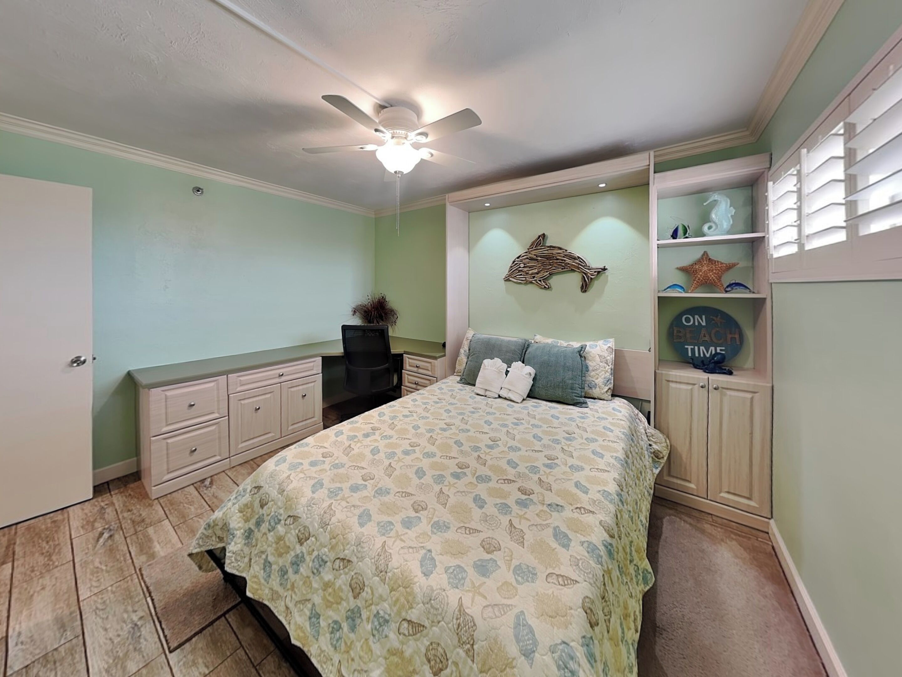 Une chambre à coucher comprenant un lit, un bureau, une chaise, un ventilateur de plafond et un mur décoré avec un motif de dauphin.