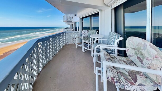 A balcony with white chairs and a table, overlooking the beach. - Oceanside Retreat 804 by Distinctive Beach Rentals (Ormond Beach)