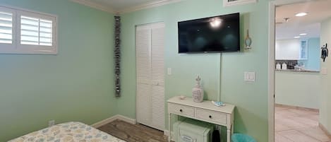 Un dormitorio con cama, cómoda, televisor y baño visible a través de una puerta abierta.