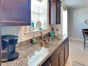 A kitchen with granite countertops, a stainless steel sink, and dark wooden cabinets. - Saltwater Escape by Ryson Vacation Rentals (Galveston)