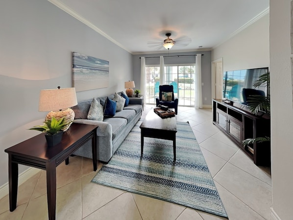 A living room with a sofa, coffee table, TV, and a ceiling fan. - Saltwater Escape by Ryson Vacation Rentals (Galveston)