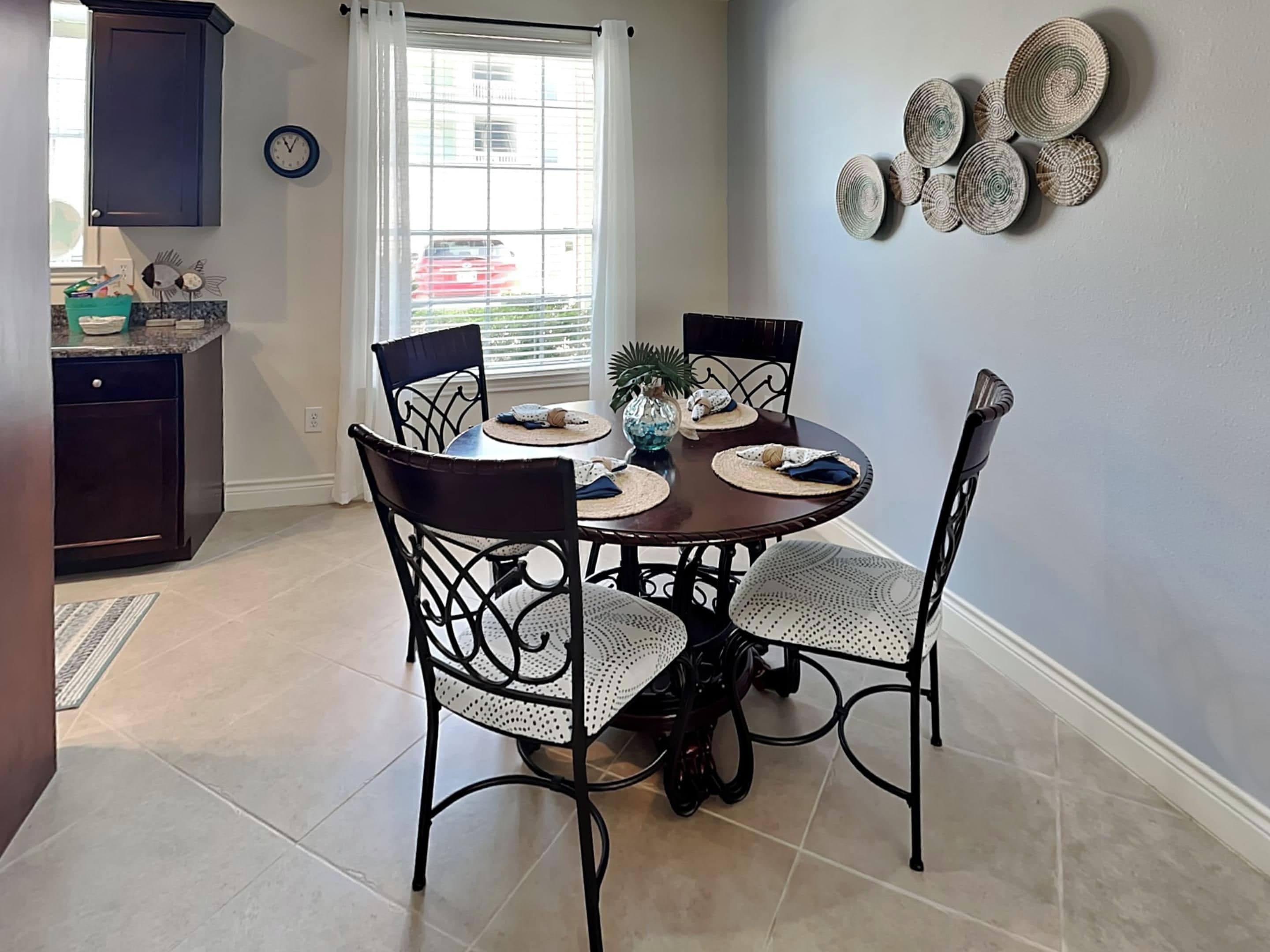 A dining area with a round table, four chairs, and a decorative wall piece.