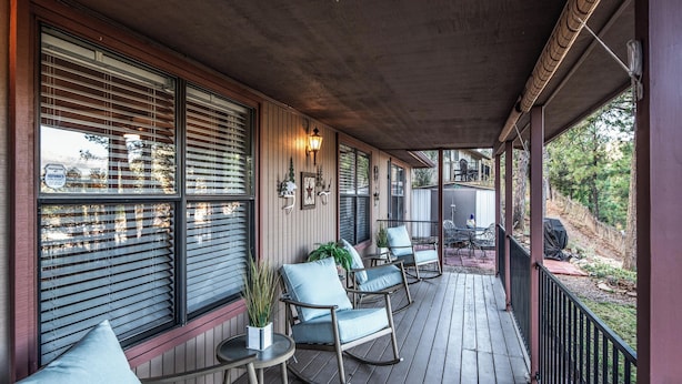 Une véranda couverte avec un plancher en bois, des fauteuils à bascule et une petite table agrémentée d’une plante.