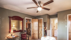 Une chambre à coucher avec un lit, un bureau avec une lampe, une chaise, un ventilateur de plafond et un miroir.
