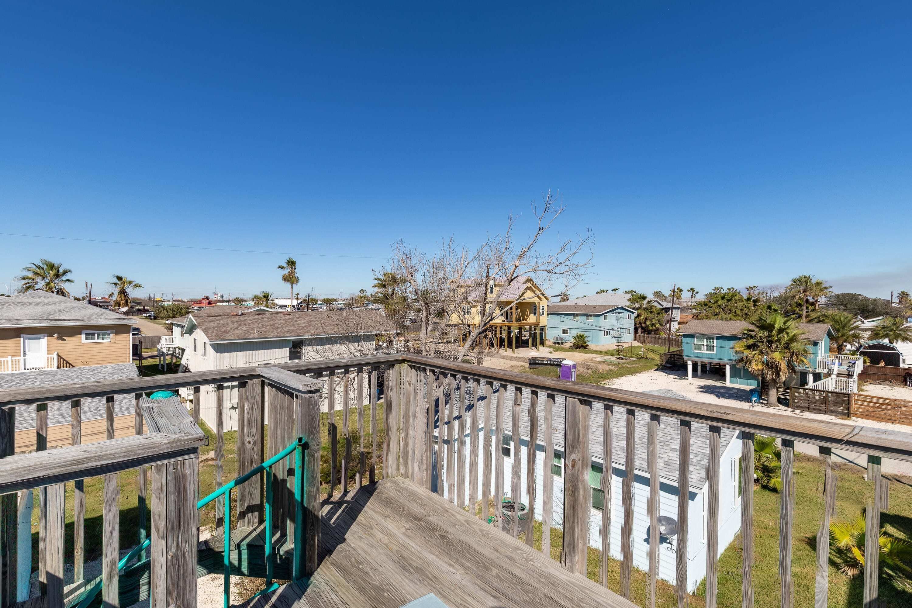 A wooden deck with a playground, overlooking a residential area with houses and palm trees.