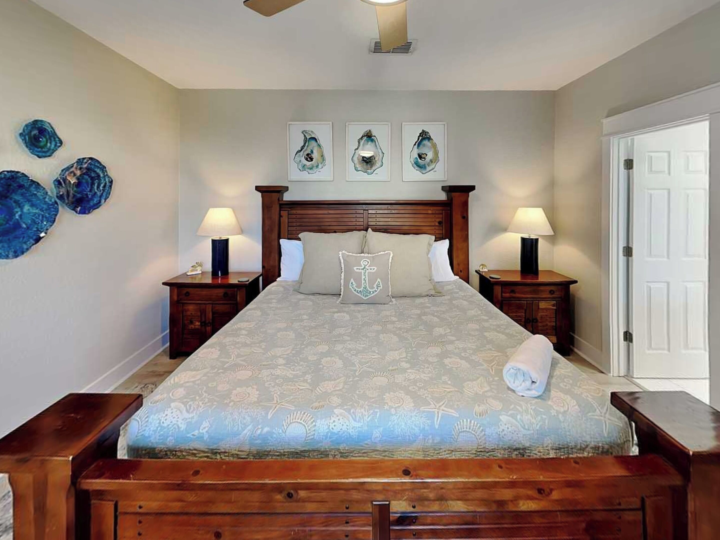 A bedroom with a large bed, wooden headboard, two bedside tables with lamps, and a door to the right.