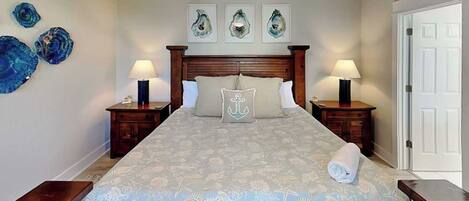 A bedroom with a large bed, wooden headboard, two bedside tables with lamps, and a door to the right.