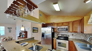 A kitchen with granite countertops, stainless steel appliances, wooden cabinets, and a built-in microwave. - Seascape Beachhouse by Distinctive Beach Rentals (St. Augustine)