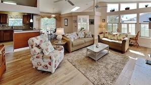 A spacious living room with a high ceiling, two sofas, a coffee table, and a dining area. - Seascape Beachhouse by Distinctive Beach Rentals (St. Augustine)