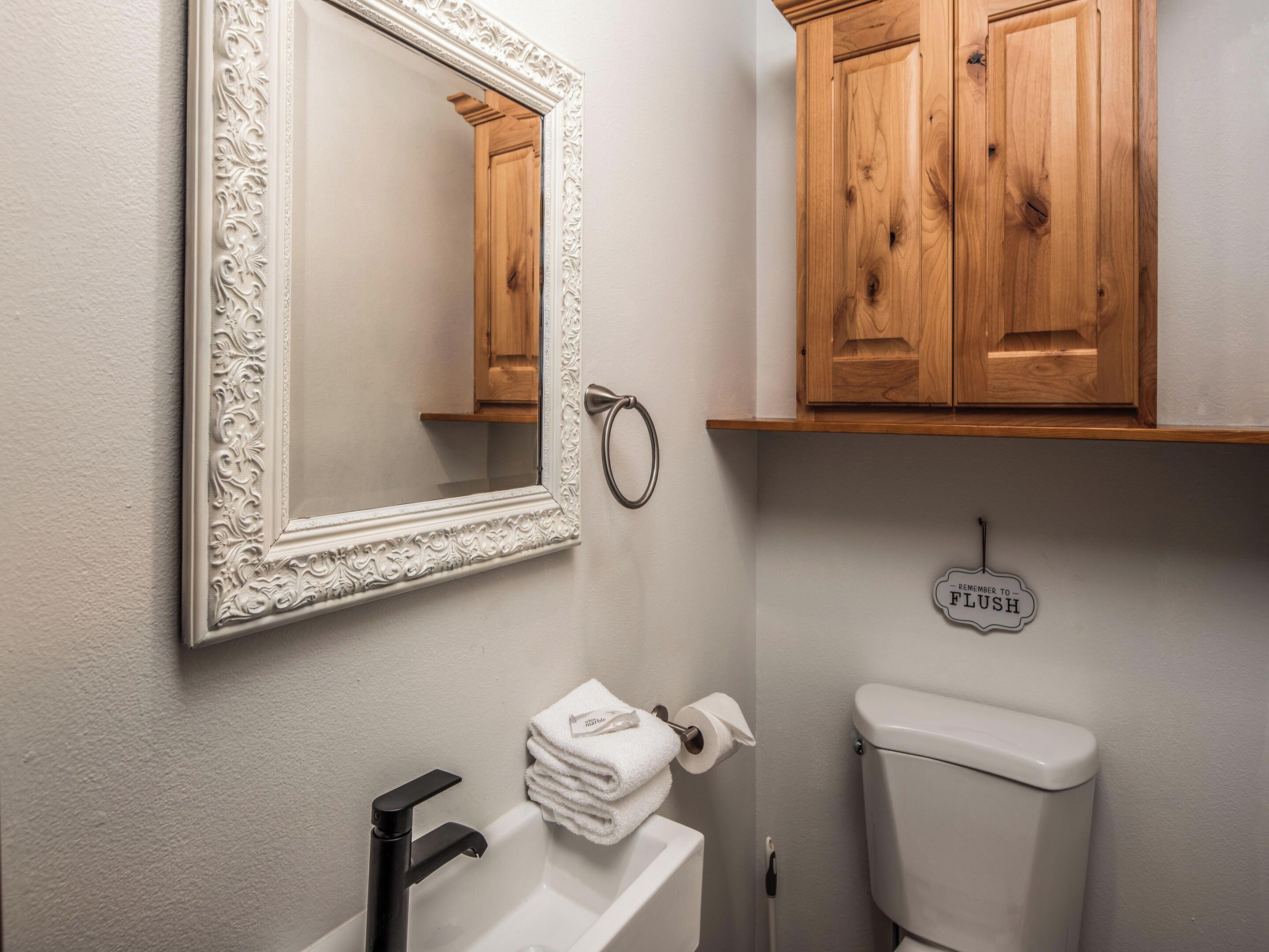 Un baño con un lavabo blanco, un espejo con un marco decorativo, armarios de madera y un inodoro.