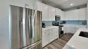 Una cocina moderna con armarios blancos, un refrigerador de acero inoxidable, un microondas y una cafetera.