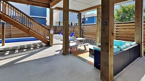 Un espacio al aire libre techado con una escalera de madera, asientos y una piscina.