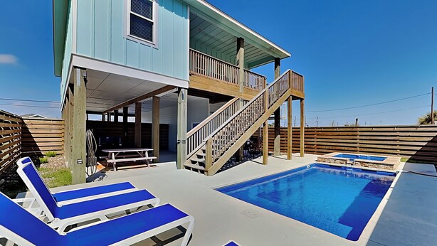 Una casa de dos pisos con balcón, piscina y sillones de descanso azules.