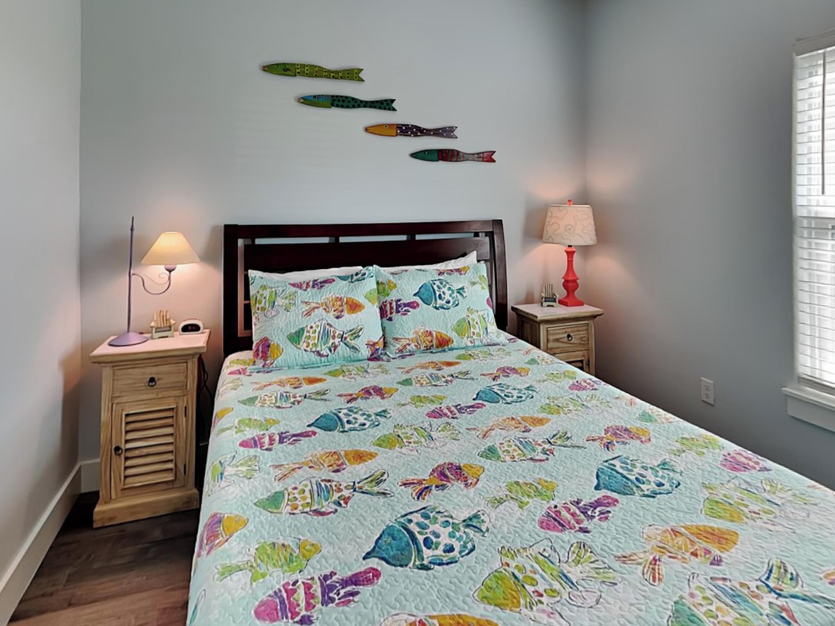 A bedroom with a bed, two bedside tables, a nightstand, a wall-mounted lamp, and a window with blinds.