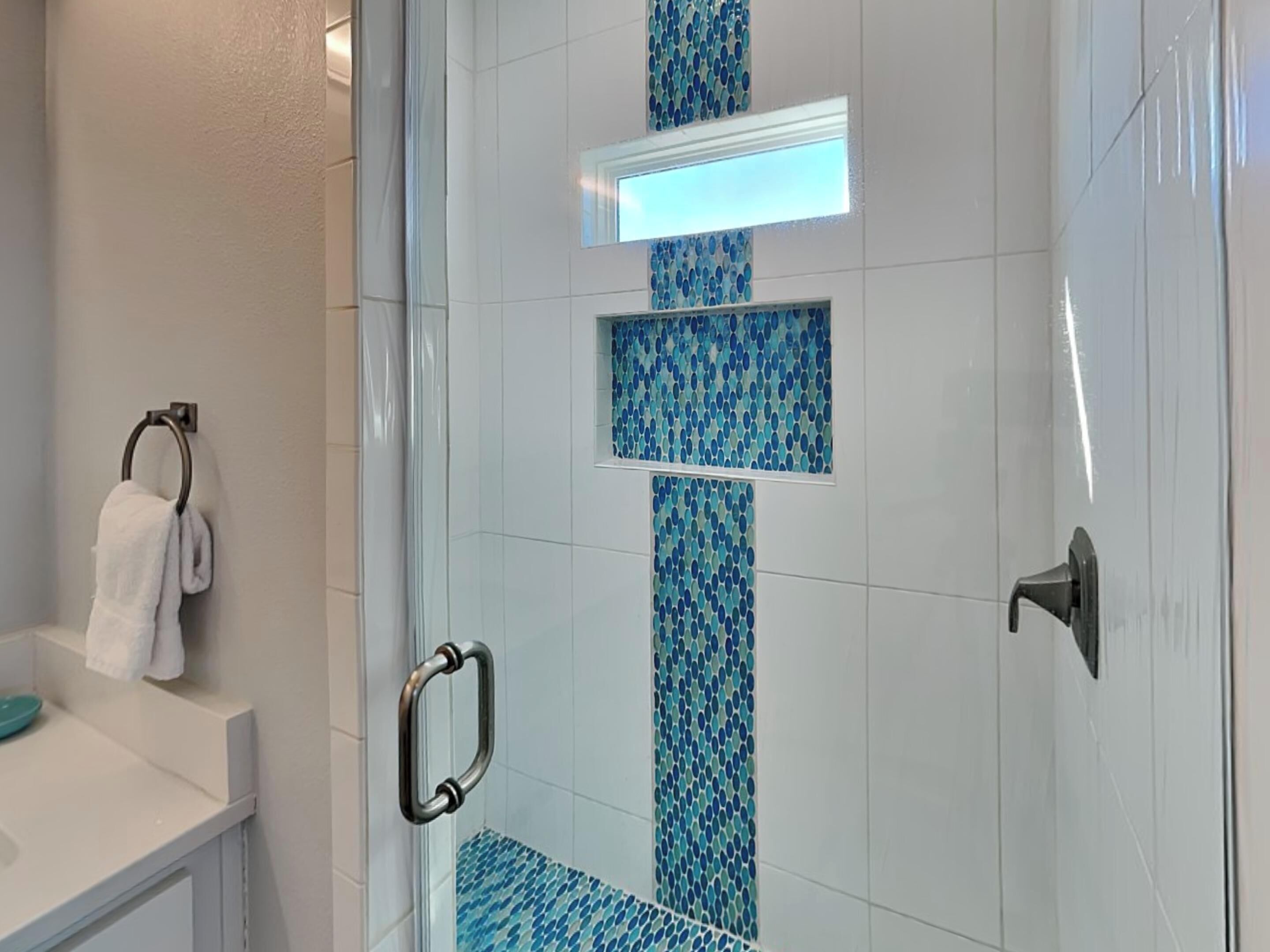 Un baño con cabina de ducha de vidrio, azulejos blancos y mosaicos azules.