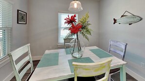 A dining area with a table, chairs, a vase with flowers, a wall-mounted fish decoration, and a window with blinds. - Mambo's Grill by Miss Kitty’s (Rockport)