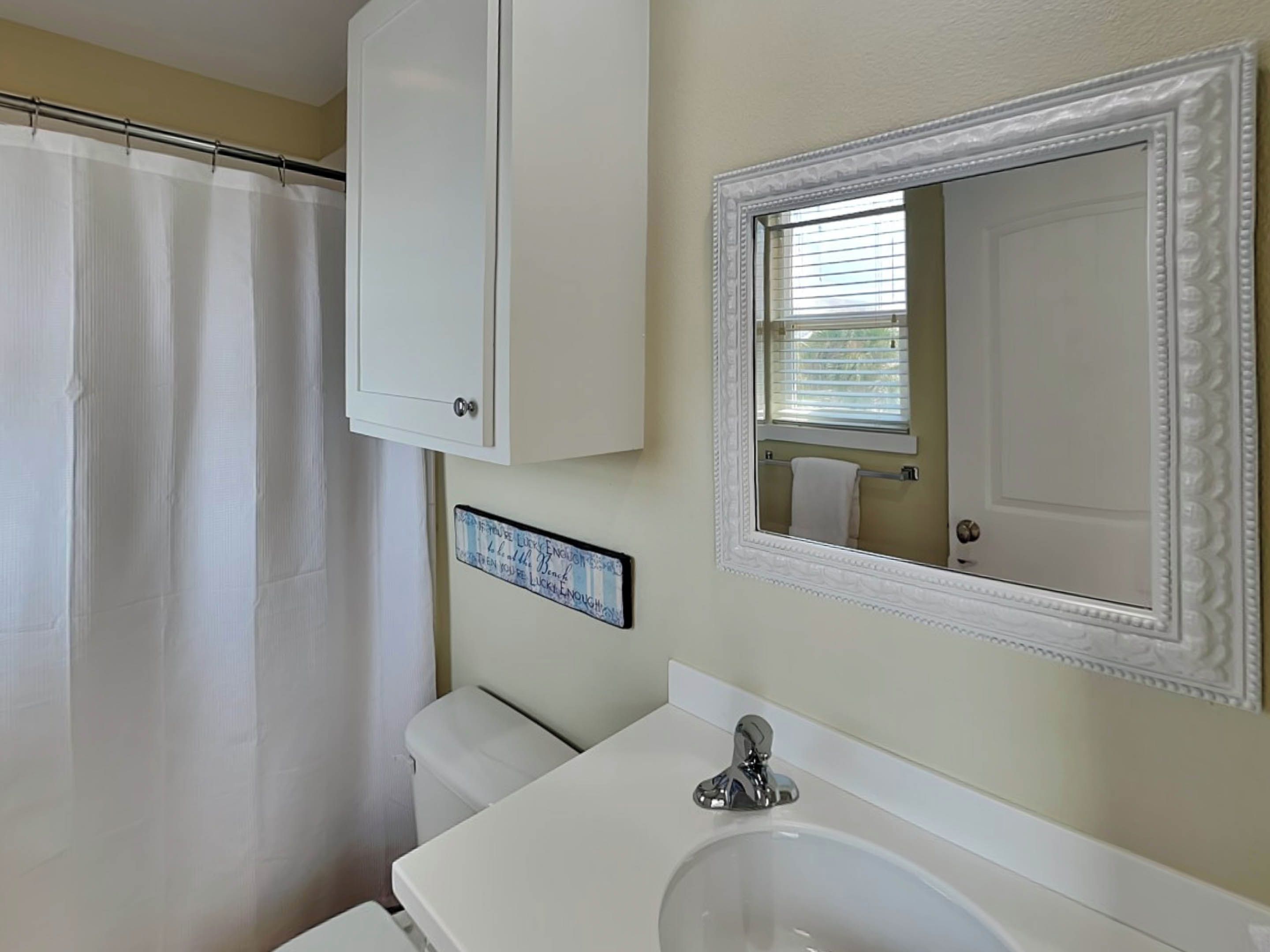 A bathroom with a white shower curtain, a cabinet, a sink with a mirror, and a towel rack.