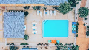 Vista aerea di un hotel con piscina, lettini e una zona coperta con sedie.