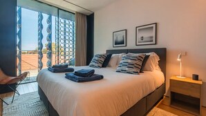Ein Hotelzimmer mit einem großen Bett, einem Sessel, einem Nachttisch und Blick durch eine Glastür.