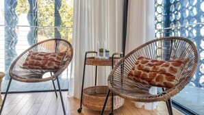 Zwei Korbstühle mit gemusterten Kissen, ein kleiner Korbstabltisch mit Kerzen und Blick ins Freie durch eine Glastür.