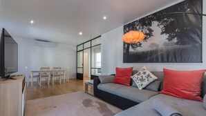 Ein modernes Wohnzimmer mit einem grauen Sofa, roten und grauen Kissen, einem großen Gemälde und einem Fernseher auf einer Holzkommode.