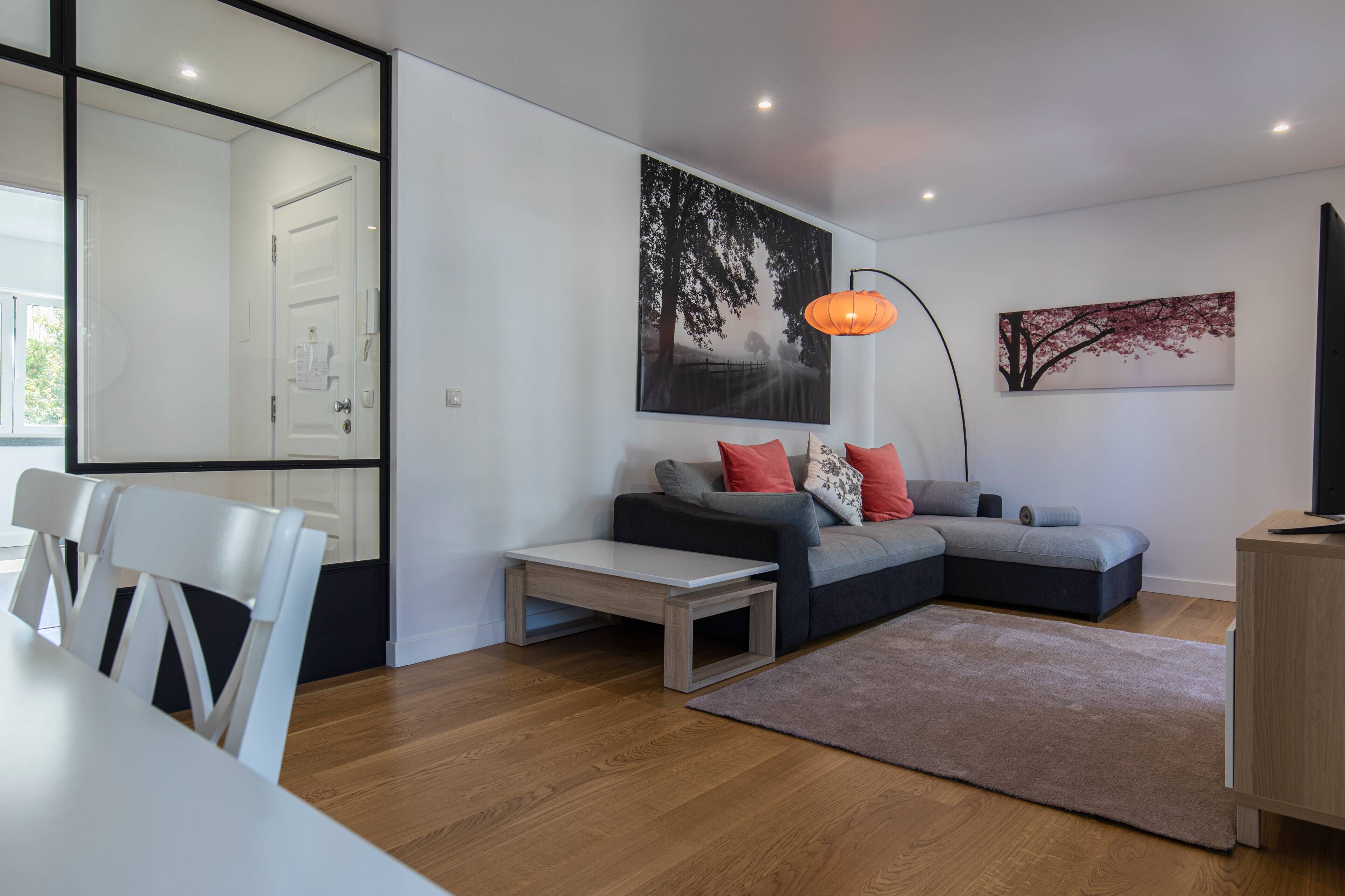 Ein modernes Wohnzimmer mit einem Ecksofa, einem Esstisch mit Stühlen, einem Couchtisch, einem Teppich und Kunstwerken an den Wänden.