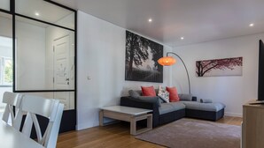 Ein modernes Wohnzimmer mit einem Ecksofa, einem Esstisch mit Stühlen, einem Couchtisch, einem Teppich und Kunstwerken an den Wänden.